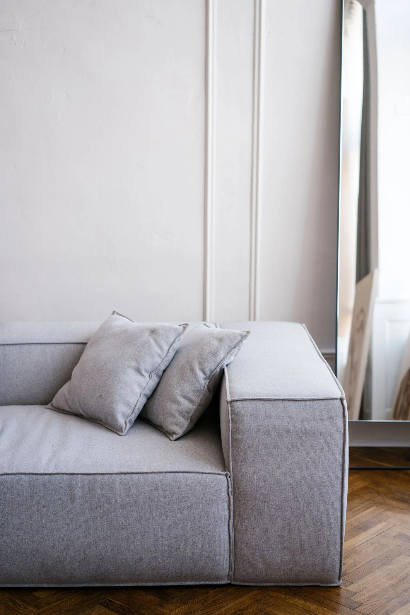 A chic gray sofa in a stylish, minimalist living room with a large mirror and elegant decor.