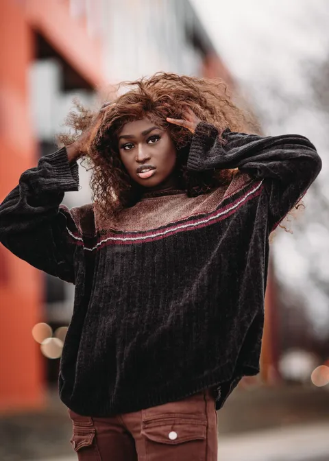 A woman wearing a dark textured sweater on an urban sidewalk.