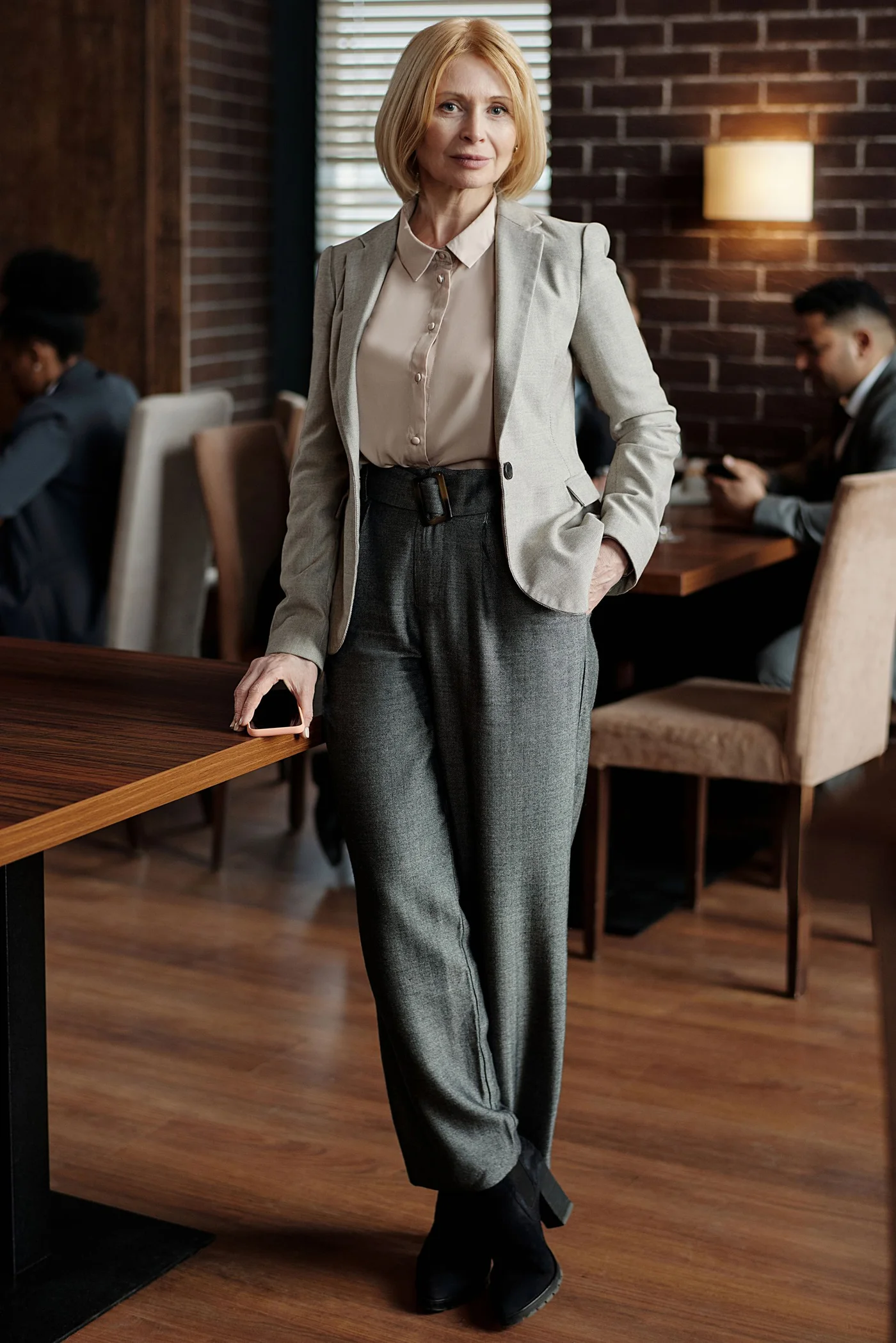 A woman in a beige blazer and gray trousers beside a cafe table.