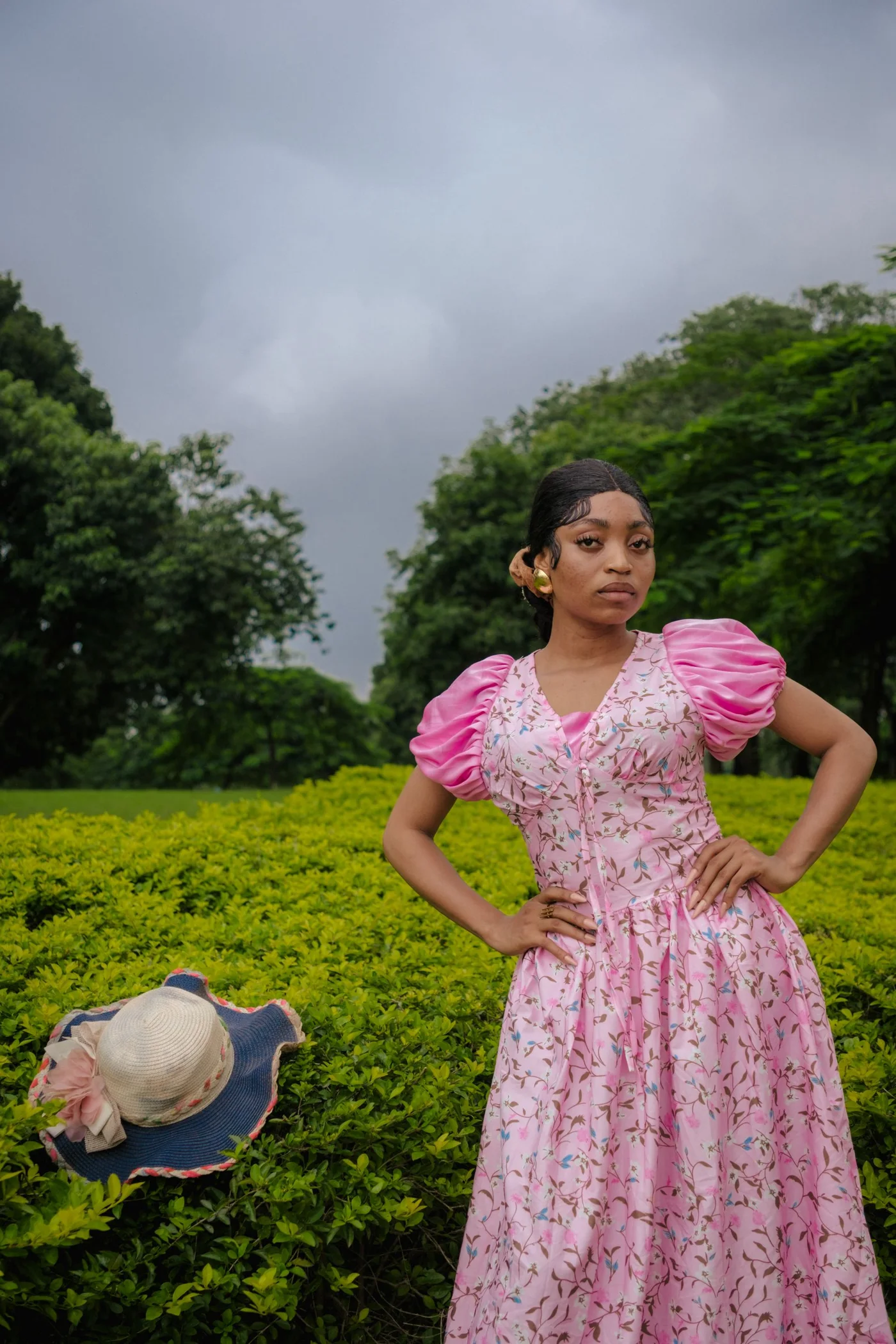 A woman wearing a pink floral dress in a leafy garden.