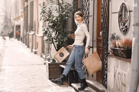 A woman in a cream blouse and jeans carrying shopping bags along a city street.