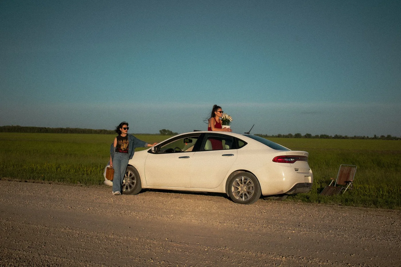 Two women standing beside a white car during a countryside road trip.
