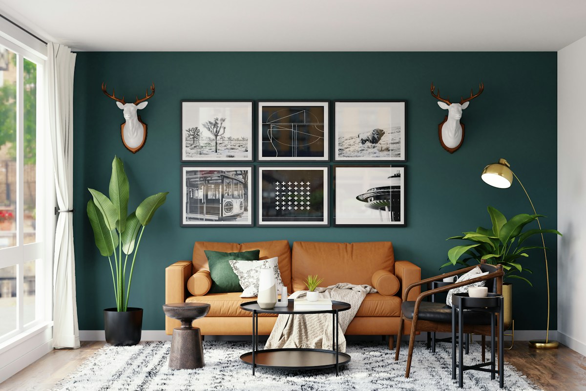 A tan sofa and framed pictures against a dark green wall