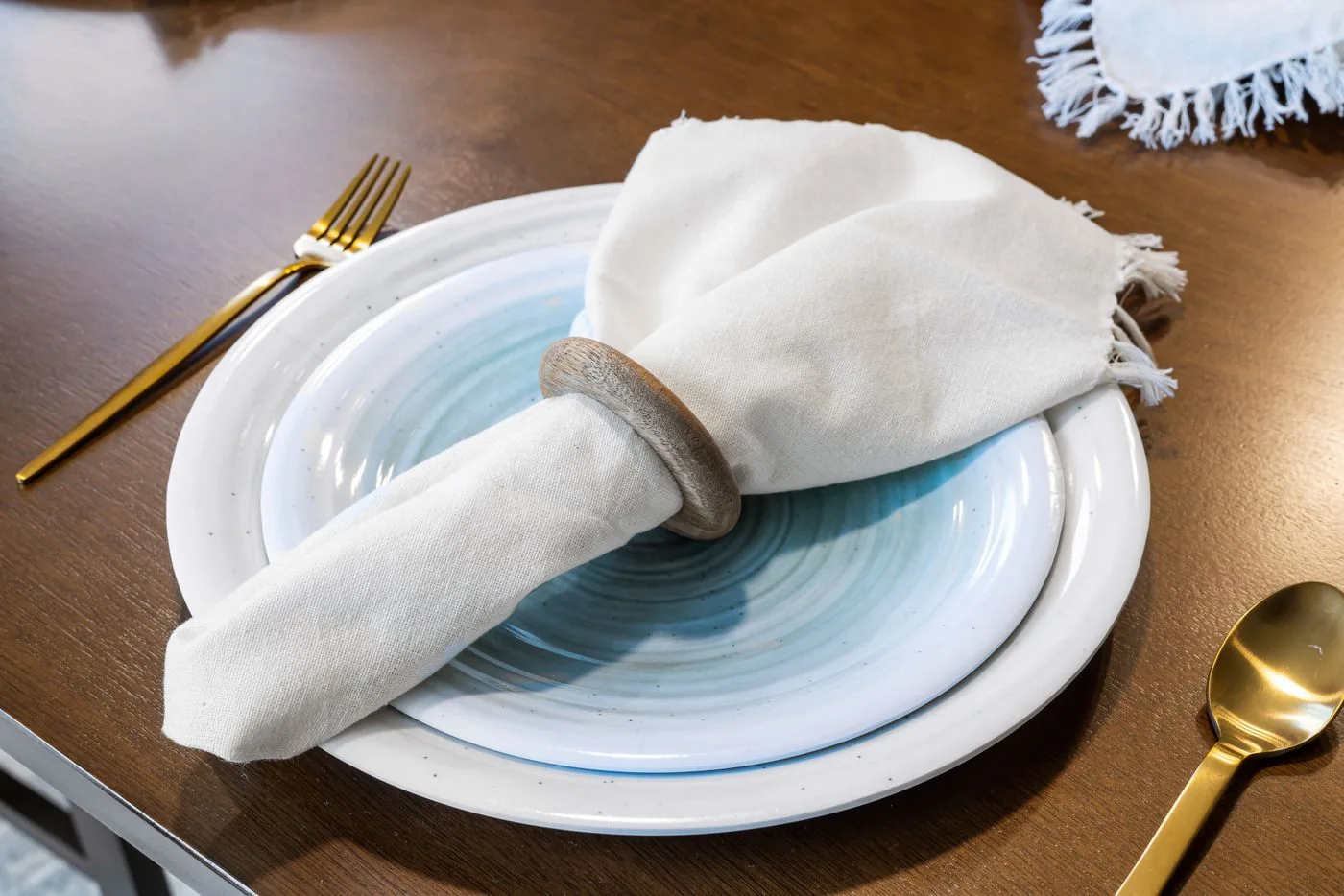 Pale plates and a light cloth napkin with gold-toned cutlery on a table