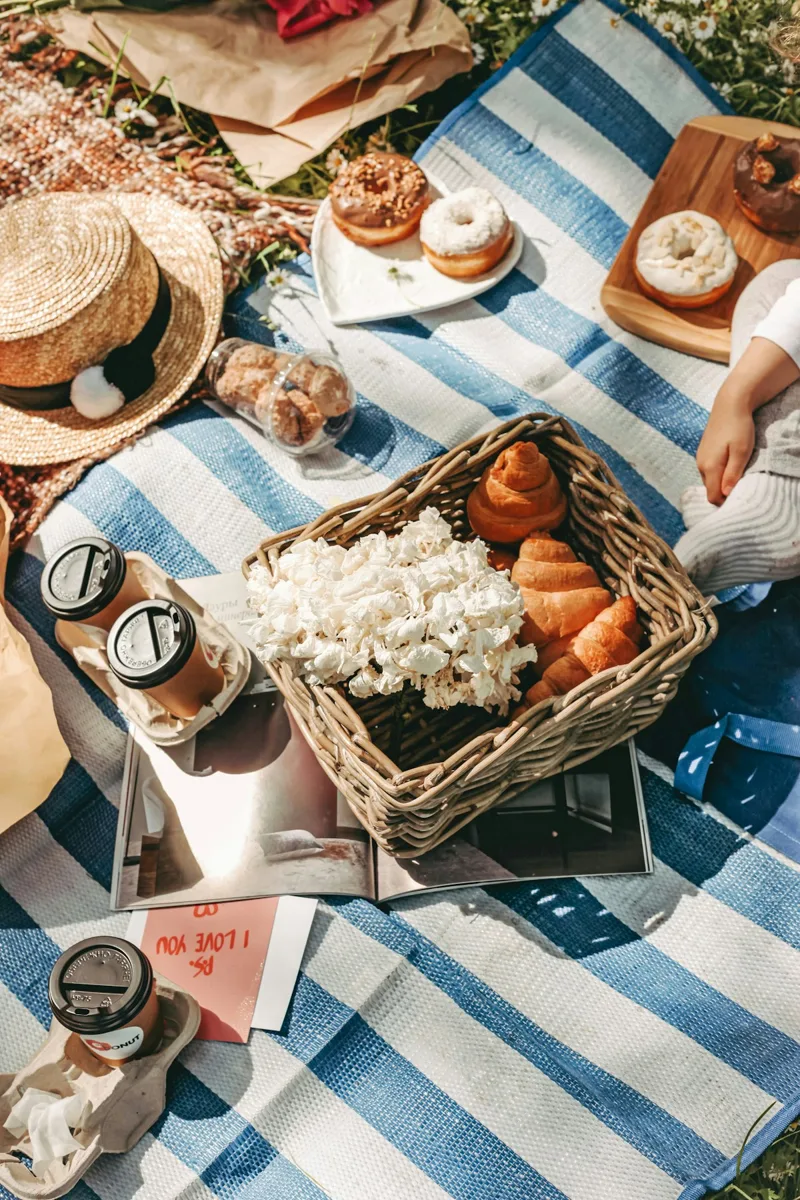 A picnic basket with bread and fruit on a striped blanket