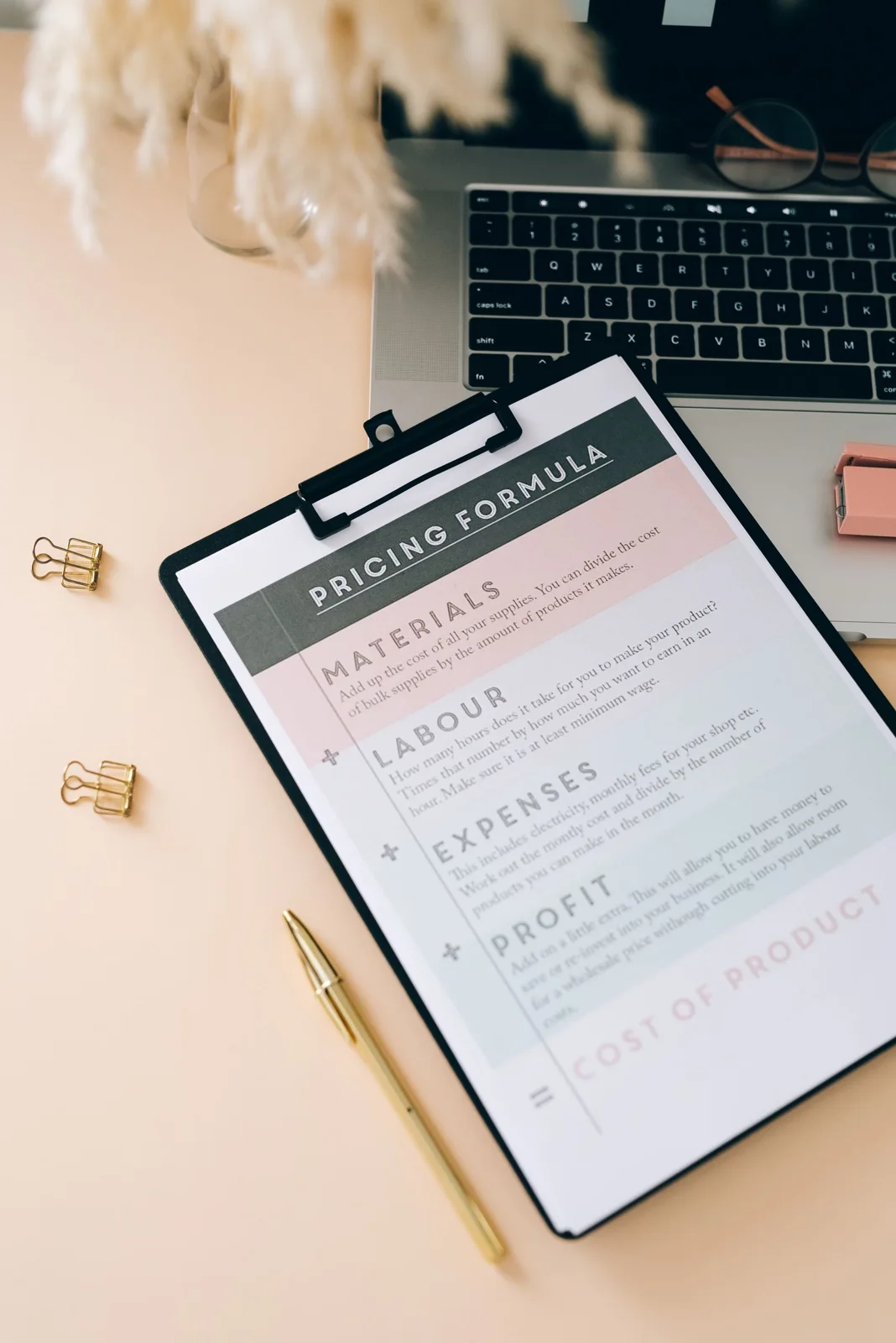 A clipboard with a printed pricing form beside stationery and a laptop