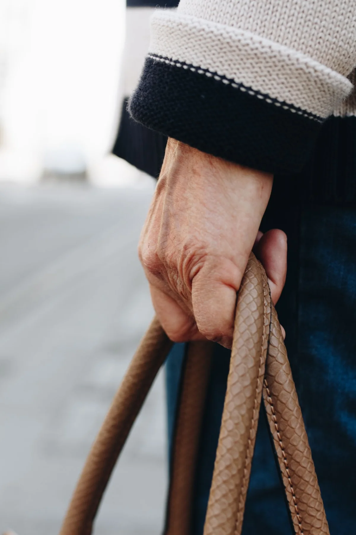 Close-up of a hand carrying a textured tan handbag outdoors