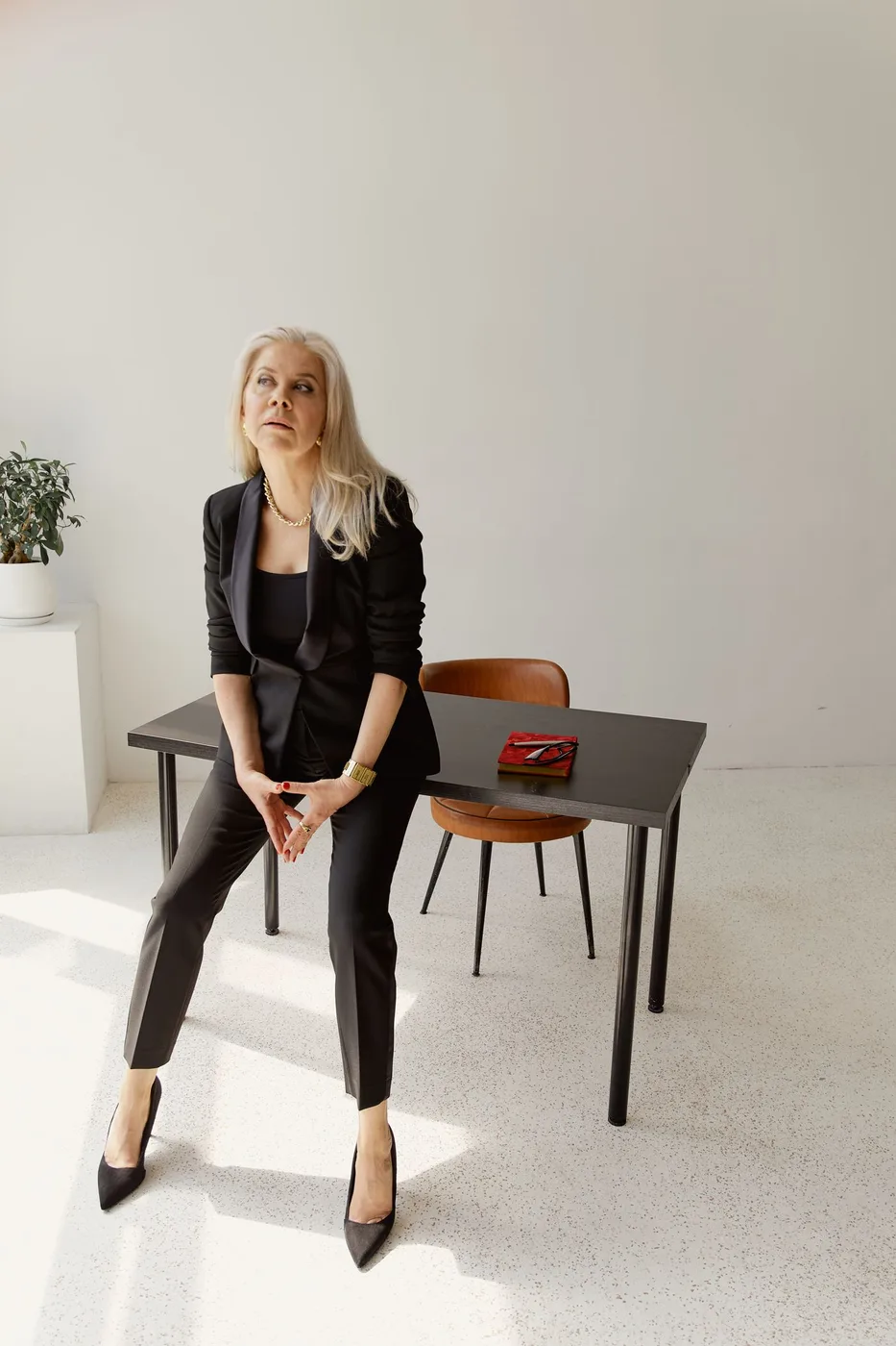 Woman wearing black tailoring seated beside a table