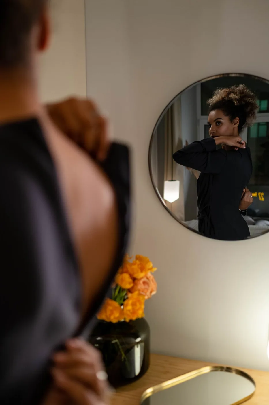 Woman adjusting a dress in front of a round mirror