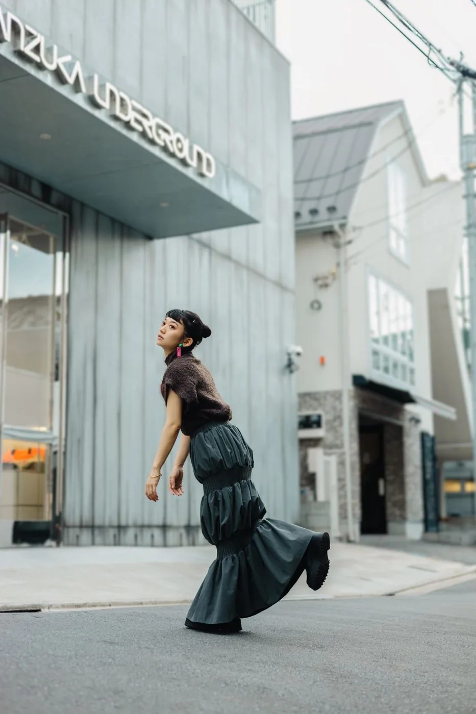 A woman wearing a dark pleated skirt and dark top on a city street
