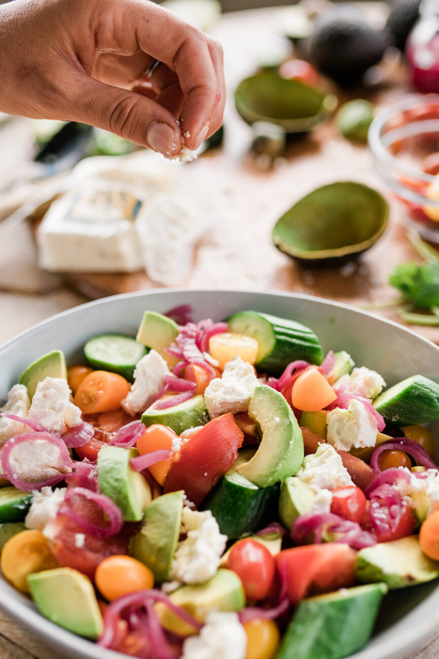 sprinking cheese on tomato, avocado, and cucumber salad