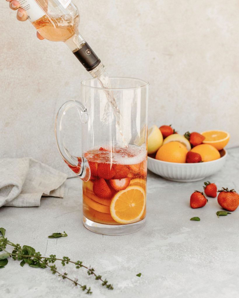 Pitcher of strawberry rosé sangria recipe next to a bowl of strawberries and oranges