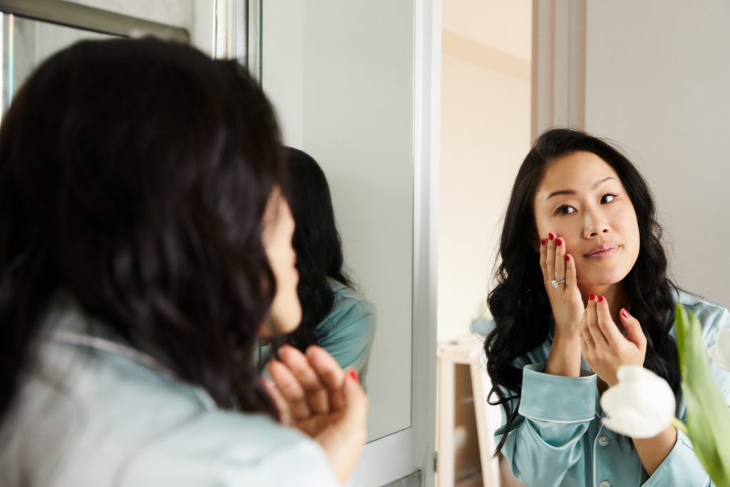 woman patting on skincare in mirror_best way to apply skicnare