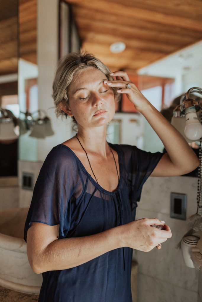 Blonde woman wearing dark blue gauzy dress doing facial massage.