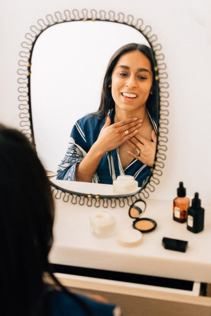 Woman applying skincare products in front of mirror.