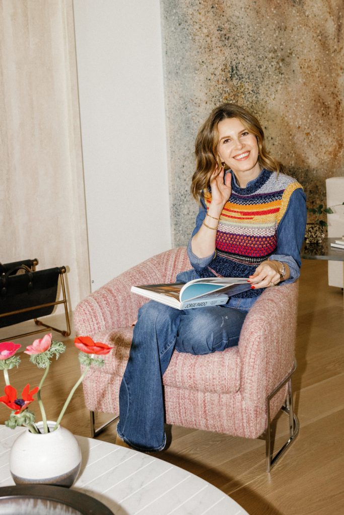 Brunette woman sitting in pink armchair reading design book.