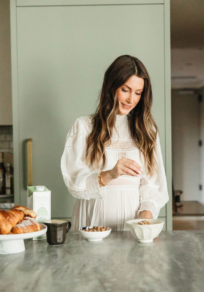 Woman with long brown hair preparing oatmeal in white bowl in kitchen.