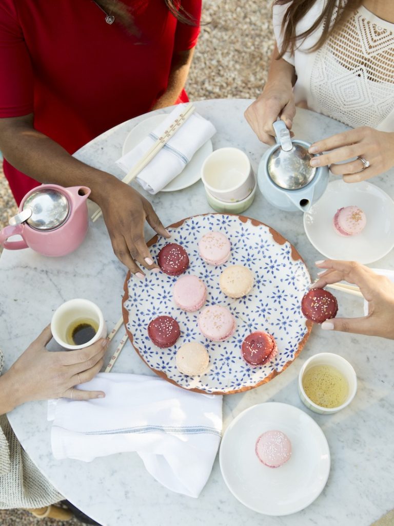 Women eating pastel-colored macarons and drinking coffee on marble-topped table at Elizabeth Street Café in Austin, Texas.