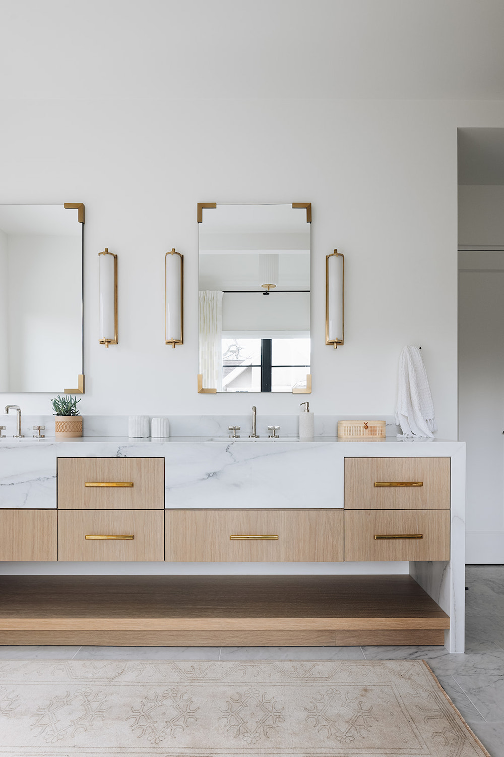 White modern bathroom with his and hers sinks, marble countertop, and light wood drawers.