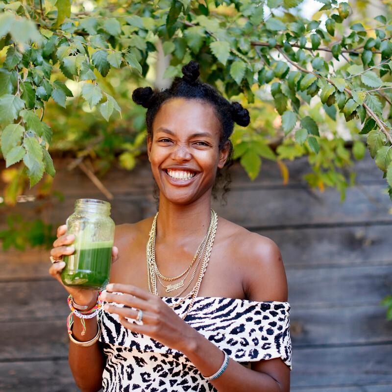 Black woman holding green juice while smiling_foods for glowing skin