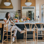 Woman sitting at kitchen island counter drinking coffee.