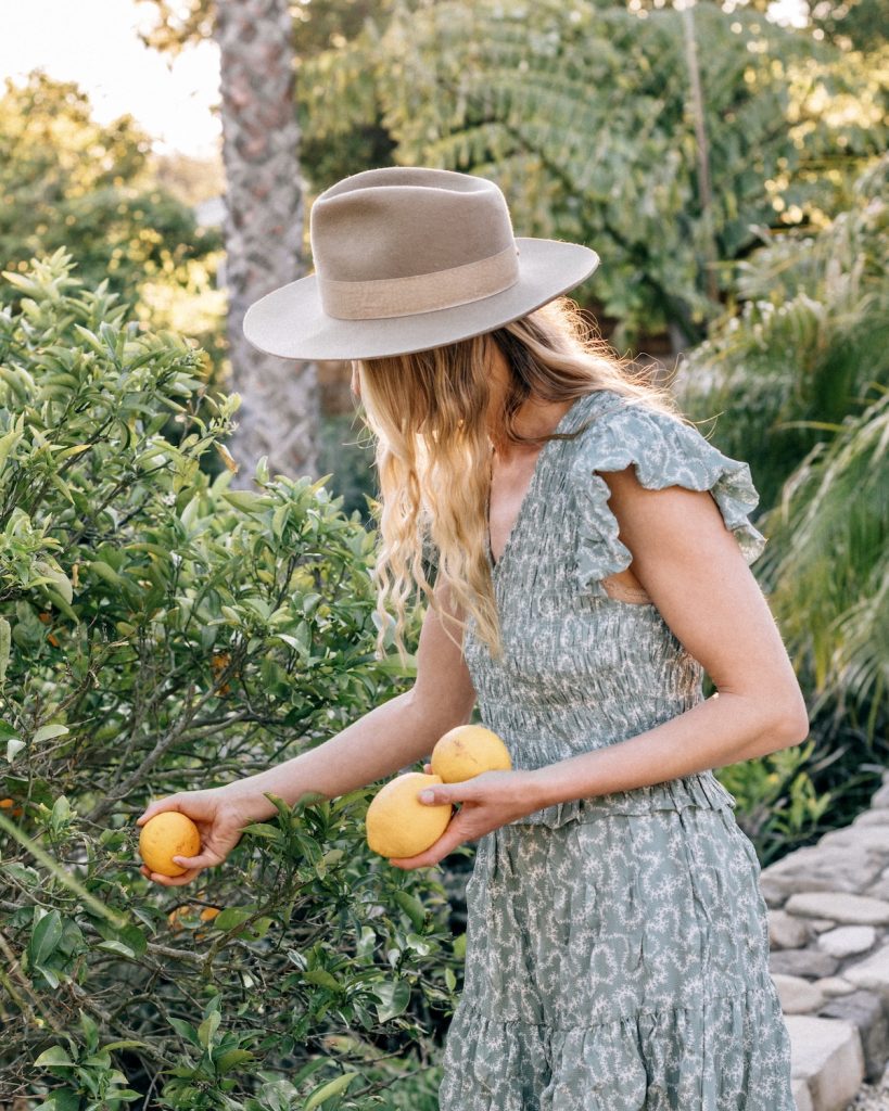Woman wearing sun hat picking lemons outside.