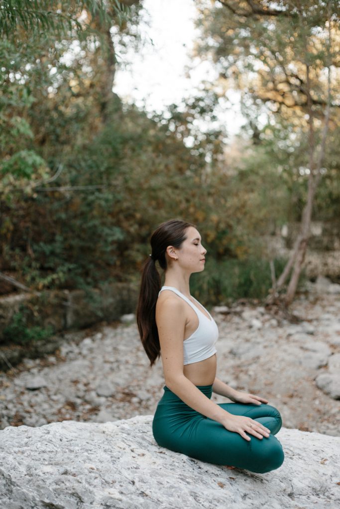 Woman meditating on rock outside.