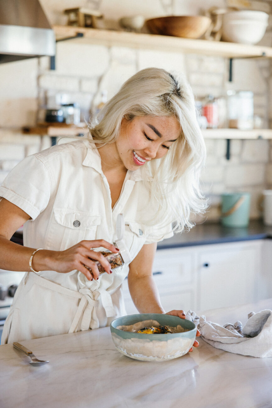 Woman adding seasoning spice to bowl.