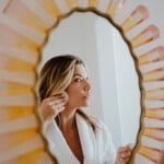 Woman applying makeup in mirror.