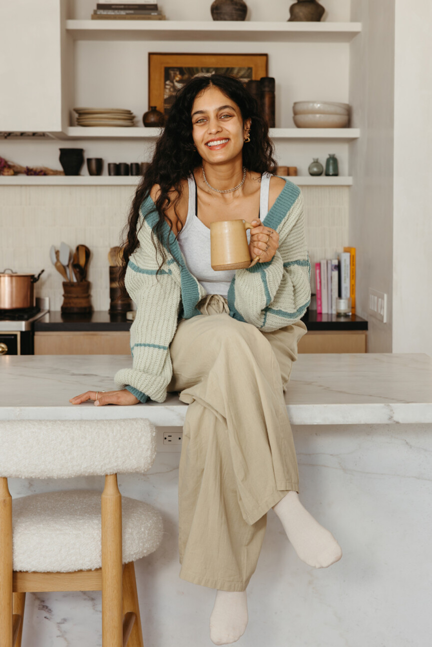 Woman drinking tea sitting on kitchen counter.