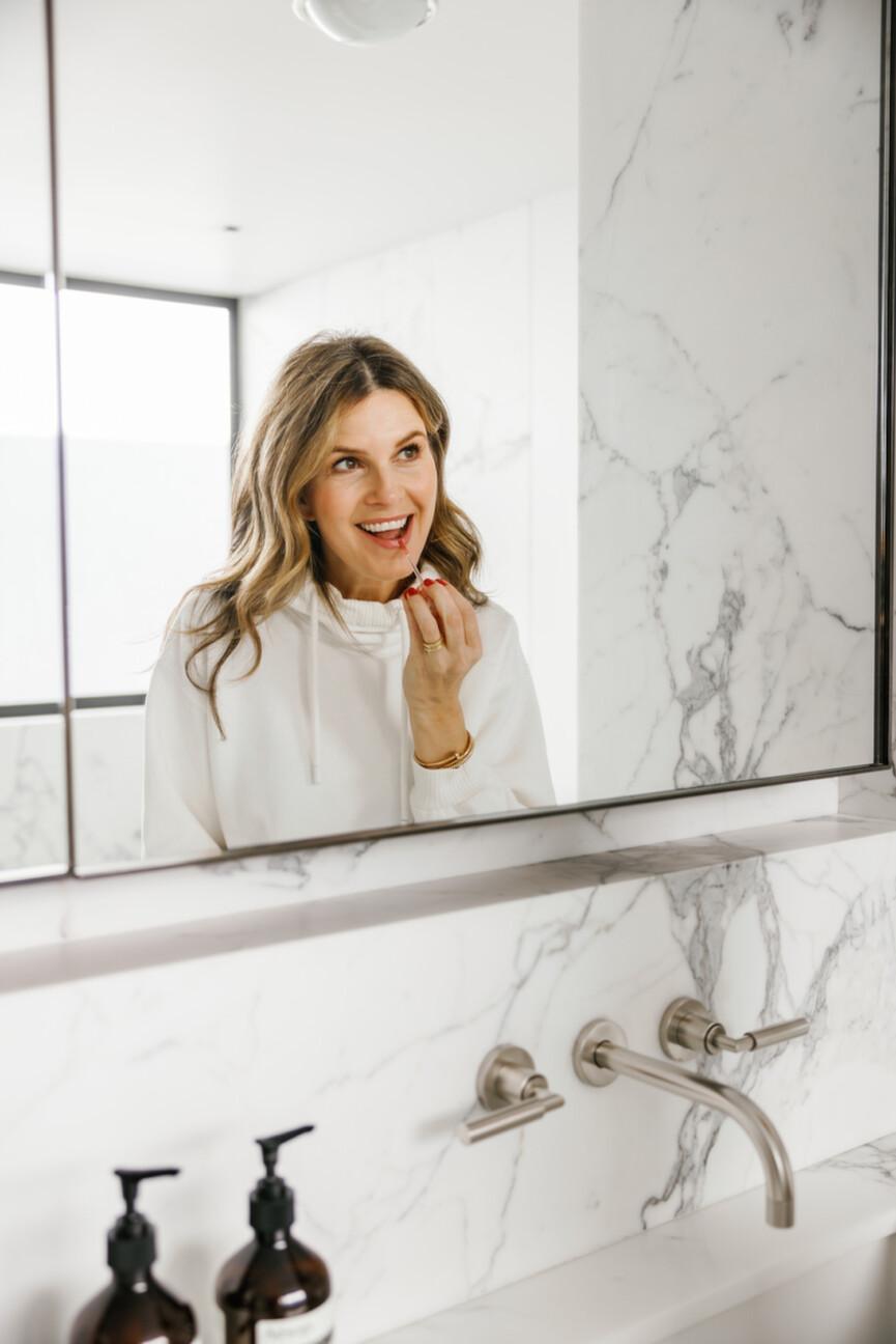 Woman applying lip gloss in mirror.
