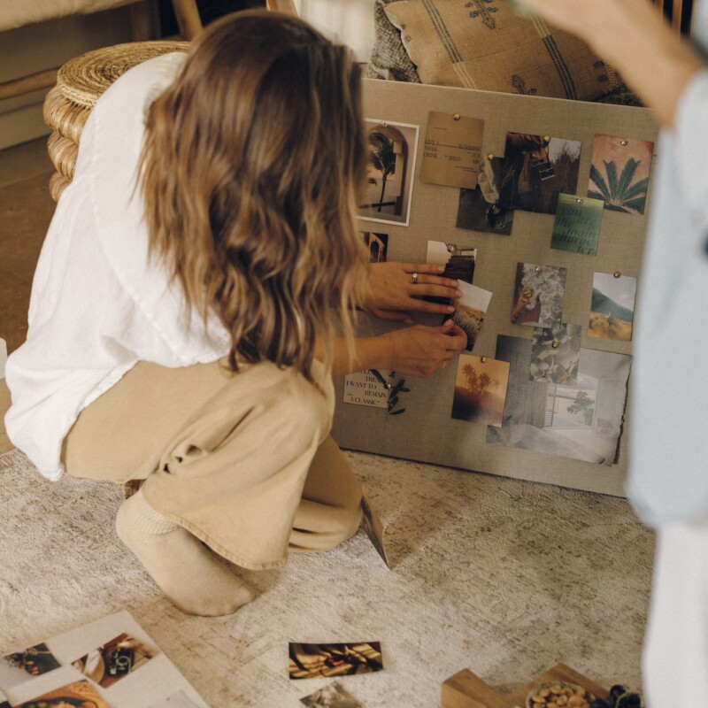 Hands pinning photos and quotes to a linen vision board
