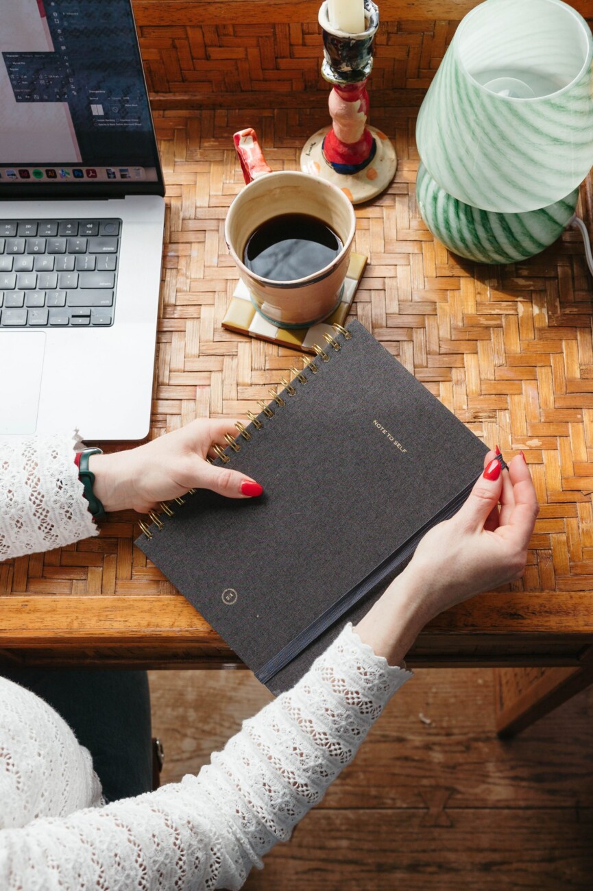 hands holding notebook on desk with computer and coffee
