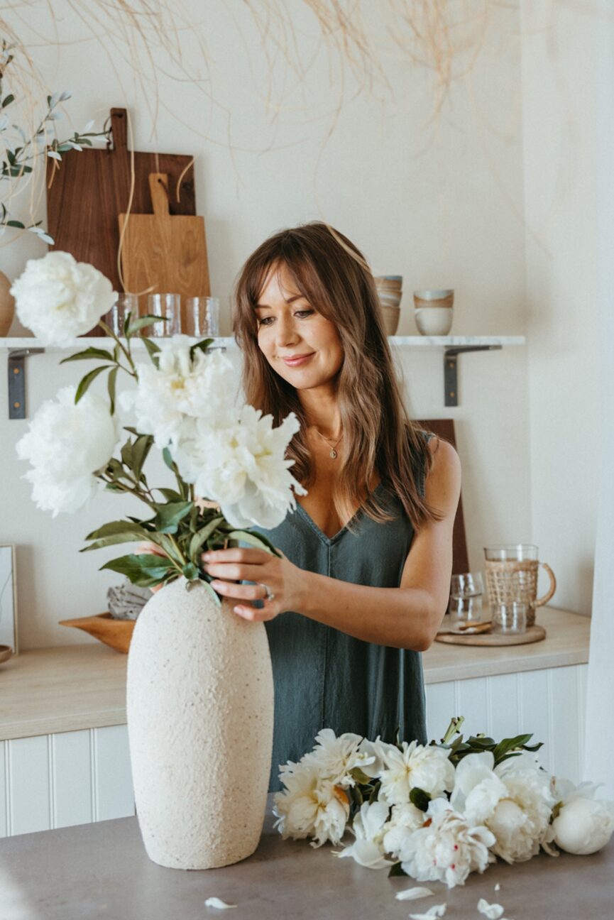 Camille Styles arranging white peonies in a vase.