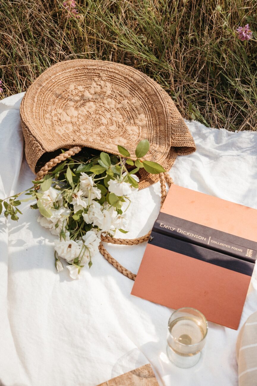 Best memoirs on picnic blanket beside flowers and a glass of wine.