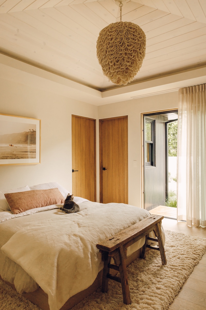 Camille Styles’ daughter’s bedroom with neutral linen bedding, a woven pendant light, and doors opening to the patio.