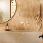 Powder bathroom vanity with warm tile, a round mirror, integrated sink, and wall-mounted brass fixtures.